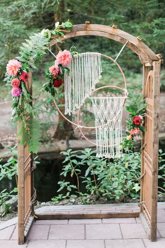 a wooden arch with leaves, flowers and macrame hangings