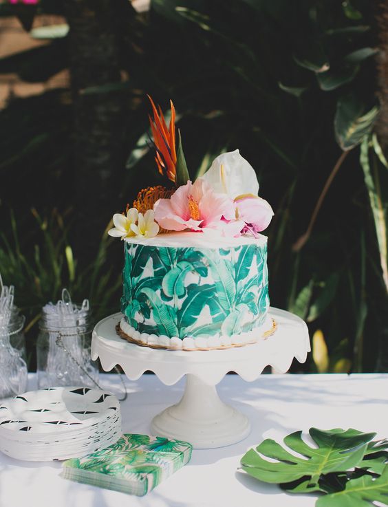 a banana leaf wrapped cake, paired with hibiscus, bird of paradise, and monstera leaves