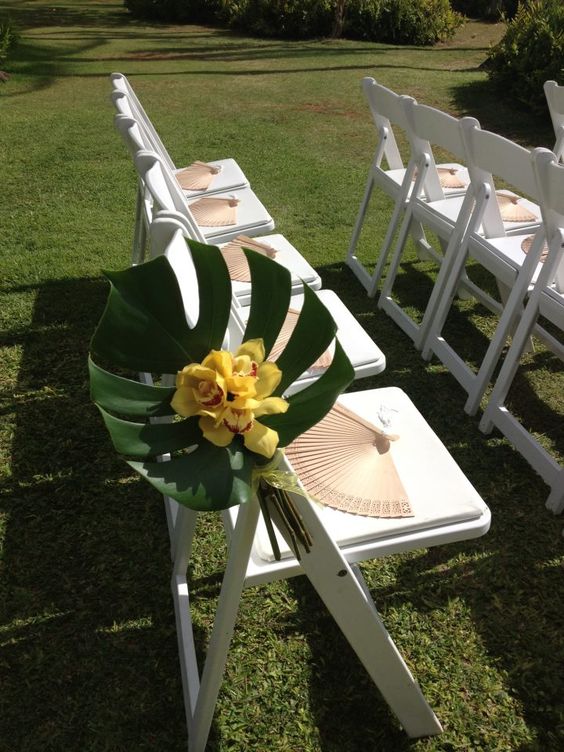 a simple pop of color with monstera leaves and orchids line the aisle with fans to help keep guest cool