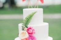 17 a plain white cake decorated with flowers and leaves and with a flamingo cake topper