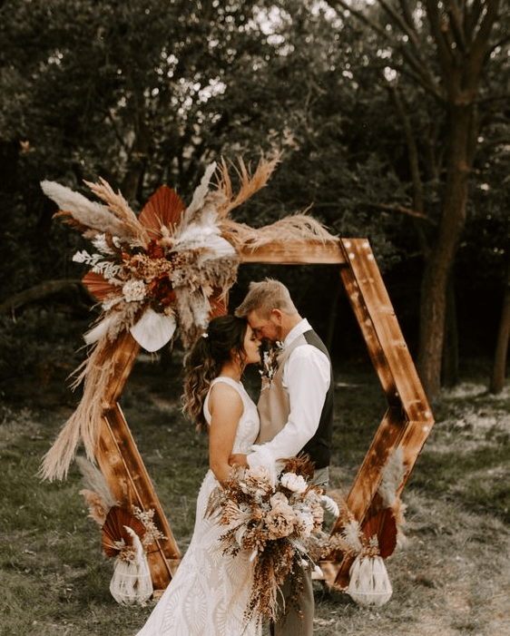 a boho hexagon wedding arch decorated with bold blooms, colorful fronds and grasses and arrangement on the ground