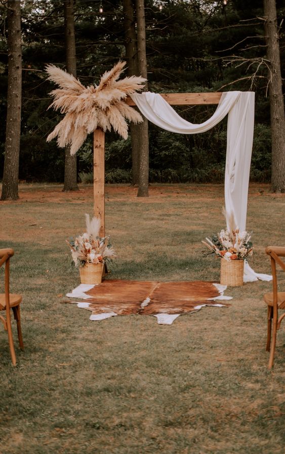 a boho meets rustic wedding arch with fabric, pampas grass, matching arrangements with grass and blooms