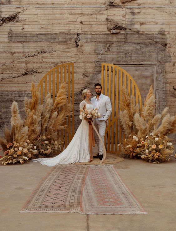 a boho wedding altar with a wooden backdrop, pampas grass, neutral and rust blooms is ideal for a boho fall wedding