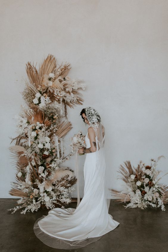a boho wedding altar with fronds, grasses, white and blush roses and baby’s breath is a unique idea for a neutral boho wedding