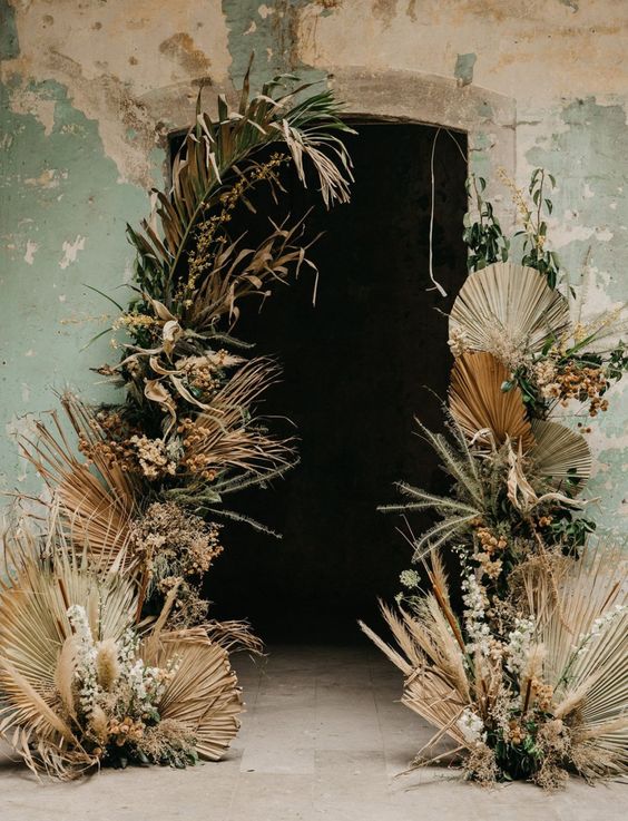 a boho wedding altar with fronds, greenery and some neutral blooms is a cool solution for a boho space