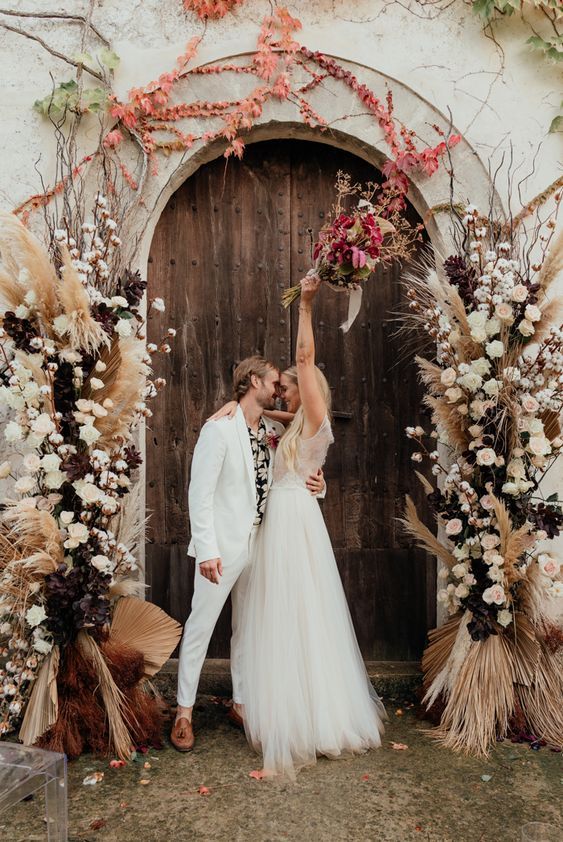 a boho wedding altar with white and blush blooms, fronds, pampas grass, twigs and cotton branches is amazing