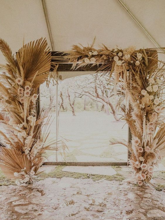a boho wedding arch with blush and white roses, fronds and pampas grass is a cool idea for a boho wedding
