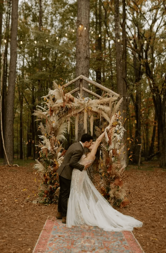 a bold boho fall wedding arch with pampas grass, bold dired fronds, greenery, colorful fall leaves and burgundy blooms inspires