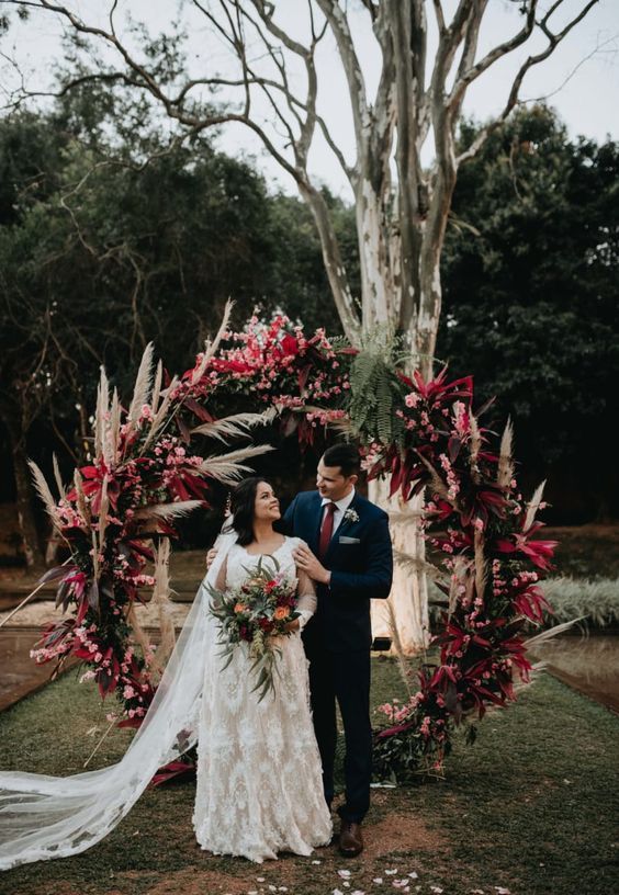 a colorful boho wedding arch with greenery, pampas grass, pink and red roses  is amazing for a boho wedding