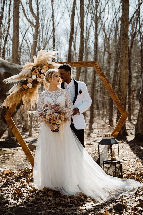 a hexagon wedding arch decorated with pampas grass, rust and white roses is a stylish idea for a fall boho wedding