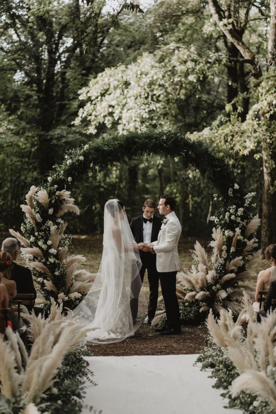 a refined boho wedding arch covered with greenery, white blooms and pampas grass is amazing