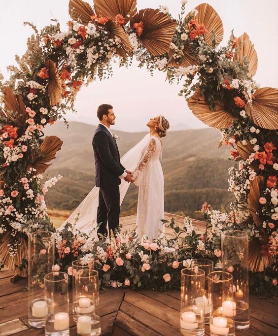 a round boho wedding arch with greenery, pink and white blooms, fronds is an amazing idea for a boho wedding