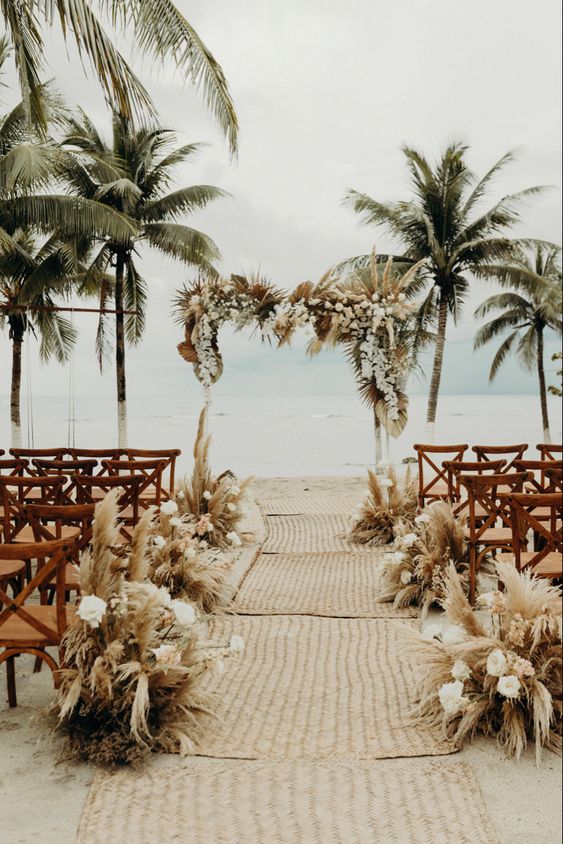 a tropical boho beach wedding arch with white orchids, greenery and pampas grass plus a lovely sea view