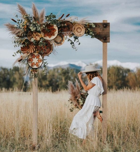 a unique boho wedding arch ith greenery, pampas grass and painted decorative baskets for a summer boho wedding