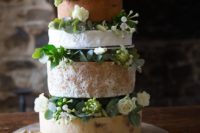 different types of cheese on a stand with fresh flowers in between the layers