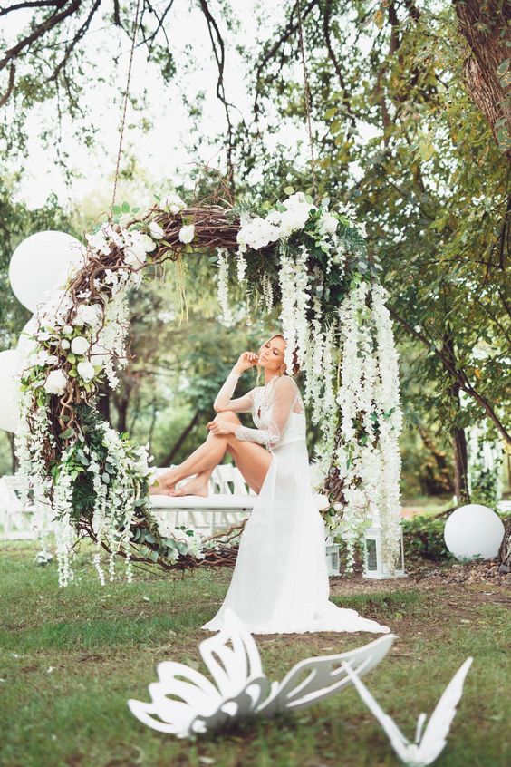 an oversized grapevine wreath with greenery and white blooms used as a swing