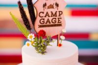 24 a plain white cake topped with wildflowers and a camp sign