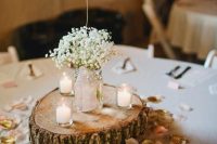 a barn wedding centerpiece of a wood slice, petals, candles and baby’s breath in a jar plus a chalkboard table number