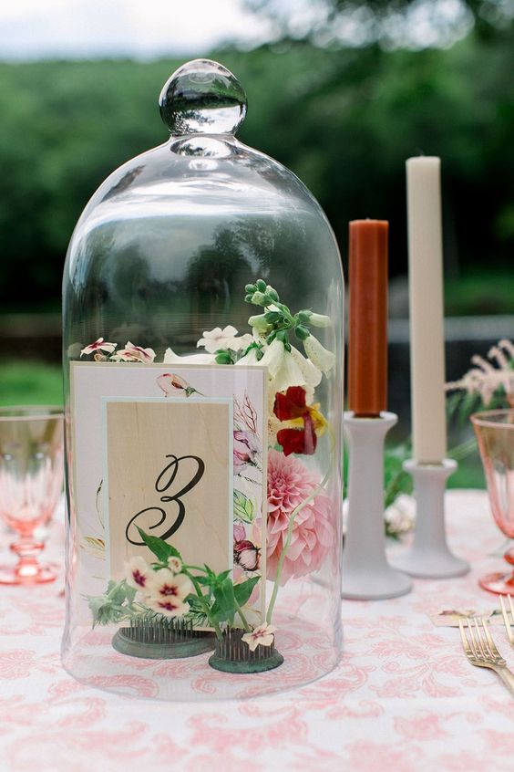 a beautiful garden wedding centerpiece of a cloche with pink and neutral blooms and a table number