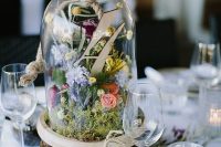 a beautiful pastel-colored wedding centerpiece of a tree slice and a cloche with pastel blooms, greenery and a table number