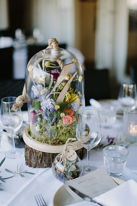 a beautiful pastel-colored wedding centerpiece of a tree slice and a cloche with pastel blooms, greenery and a table number