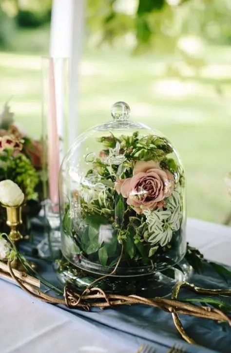 a blue table runner and a grey tablecloth, vine branches, a cloche with a pink bloom and some greenery, pink candles for an enchanted forest wedding