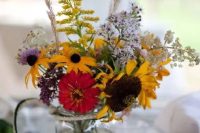 a bold floral wedding centerpiece of colorful blooms, sunflowers, lilac and yellow touches and dried grasses is amazing