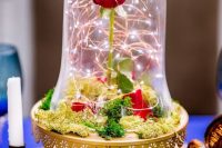 a bold the Beauty and the Beast wedding centerpiece of a gold cloche with moss, a single red rose and LEDs