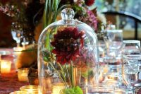 a bold wedding centerpiece of a cloche with burgundy blooms and moss inside is a super cool idea