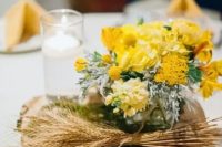 a bright rustic wedding centerpiece of a wood slice, wheat, moss and yellow blooms and pale greenery
