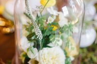 a bright wedding centerpiece of a cloche with greenery, astilbe, white and yellow blooms