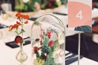 a bright wedding centerpiece of a cloche with greenery, red blooms and some smaller fillers
