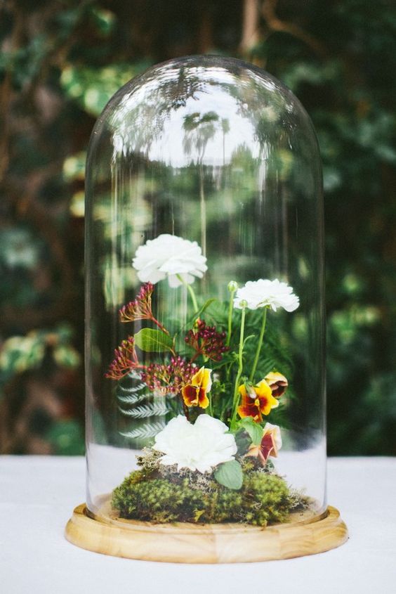 a bright wedding centerpiece of a cloche with moss, fern and some white and bold blooms is a cool idea for a woodland wedding