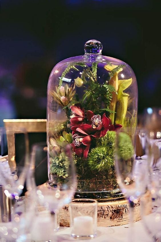 a bright wedding centerpiece with moss, greenery and bold blooms placed in a cloche