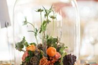 a catchy wedding centerpiece of a cloche with berries, bright blooms, an artichoke and greenery for summer or fall