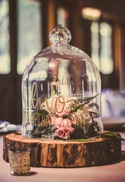 a catchy wedding centerpiece of a cloche with gold calligraphy, neutral blooms and greenery and a tree slice