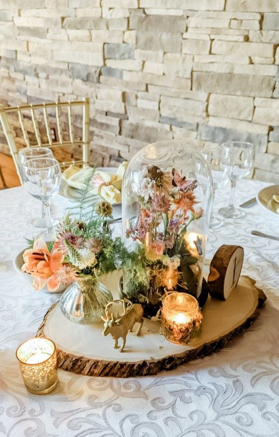 a catchy wedding centerpiece of a tree slice with a clocehw ith pastel blooms, a candle, a deer and a floral arrangement