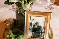 a chic barn wedding centerpiece of a wood slice, moss, some greenery and neutral blooms plus the couple’s photo