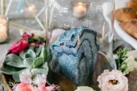 a cloche with a large blue geode and pastel and bright blooms aroudn plus greenery for a catchy wedding centerpiece