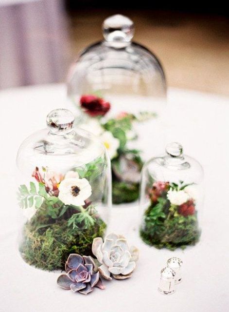 a cluster wedding centerpiece of cloches with moss, greenery and red and white blooms