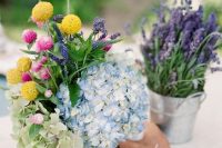 a colorful rustic cluster wedding centerpiece of buckets with hydrangeas, billy balls and lavender plus a wooden piece with a candle