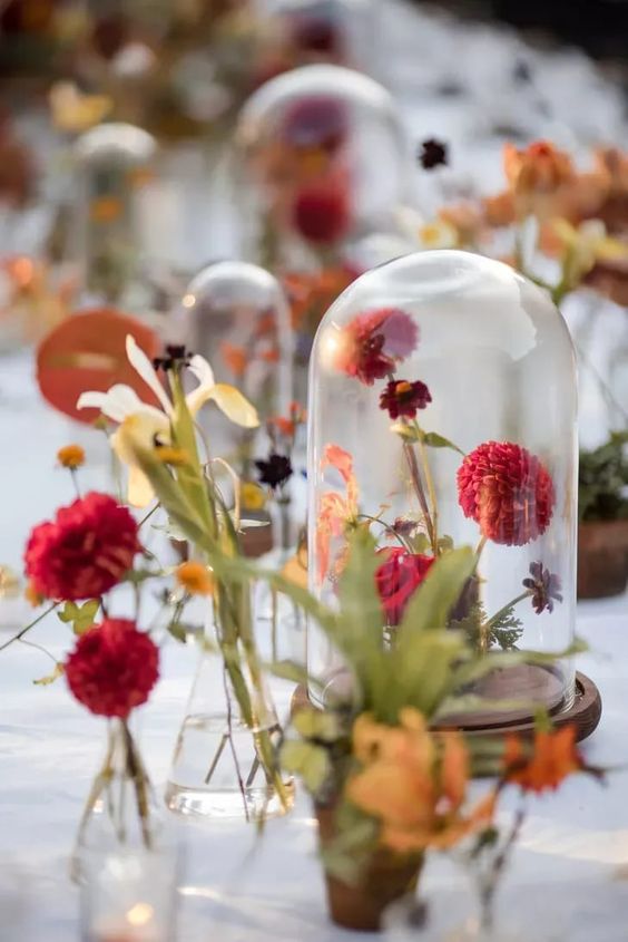 a colorful wedding centerpiece of a cloche with coral blooms and greenery and matching blooms around