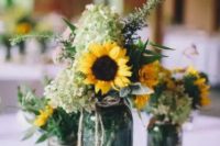 a cool rustic wedding centerpiece of jars with greenery, green hydrangeas and sunflowers plus candles around is an easy solution