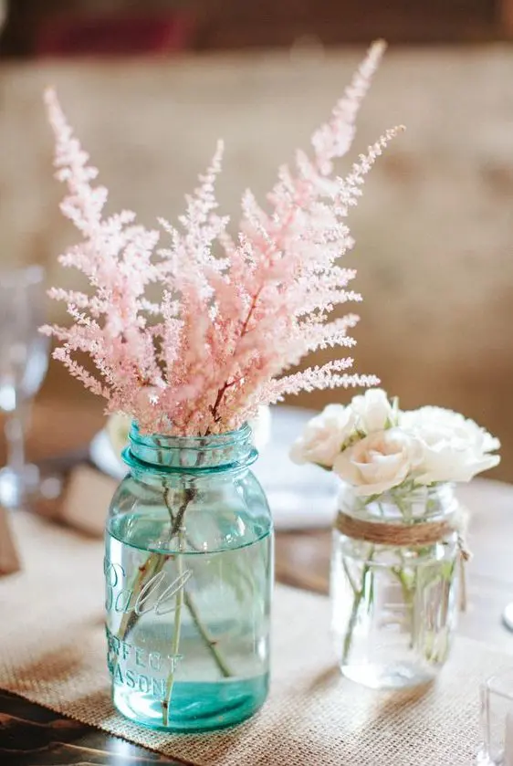 a cool wedding centerpiece of a blue jar with pink astilbe and a clear jar with small white roses for a rustic wedding