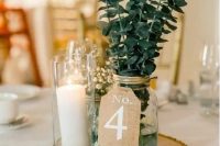 a cool wedding centerpiece of a tree slice, a pillar candle in a glass, a mason jar with eucalyptus and baby’s breath in a glass