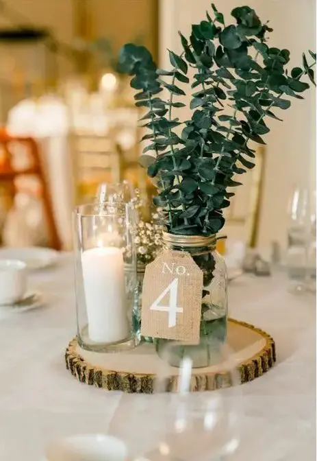 a cool wedding centerpiece of a tree slice, a pillar candle in a glass, a mason jar with eucalyptus and baby's breath in a glass