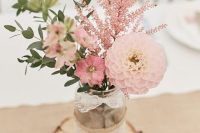 a cozy farmhouse wedding centerpiece of a jar with greenery, pink blooms and pink astilbe put on a wood slice is wow