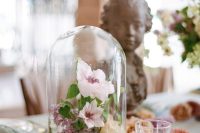 a delicate garden wedding centerpiece of a cloche with pastel blooms and leaves for a spring or summer wedding