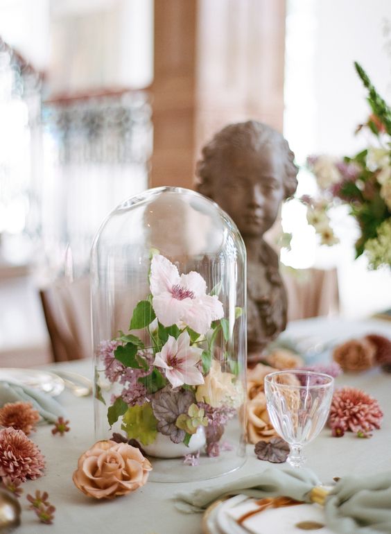 a delicate garden wedding centerpiece of a cloche with pastel blooms and leaves for a spring or summer wedding