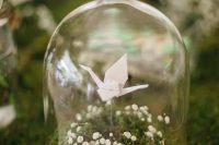a delicate wedding centerpiece of a cloche with moss and baby’s breath and a single white paper crane is a lovely idea